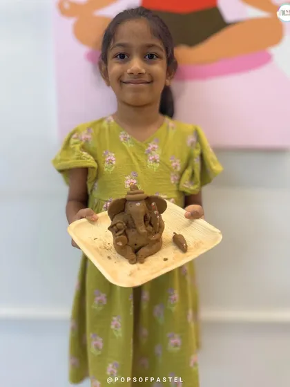 The proud smile of a young artist holding her finished clay Ganesha. Our workshops are designed to build confidence and let little hands create big, beautiful things.