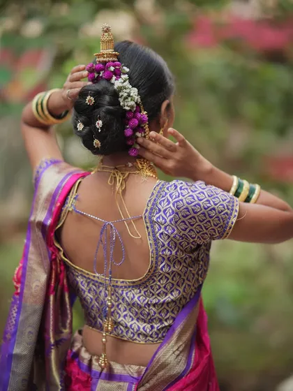 The classic Khopa bun is essential for a traditional Maharashtrian bride. Here, I've adorned it with fresh purple and white flowers and delicate hair accessories for a truly royal touch. This is a hairstyle that is both elegant and secure.