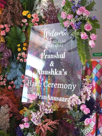 The personalized welcome sign for the Haldi ceremony, framed by a lush arrangement of colorful flowers. This is the first beautiful detail guests see as they arrive.