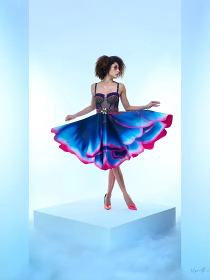 A full-length shot from a designer campaign, featuring a flowing blue and pink dress. The model's pose creates a sense of graceful movement, perfectly captured with studio smoke effects for a magical atmosphere.