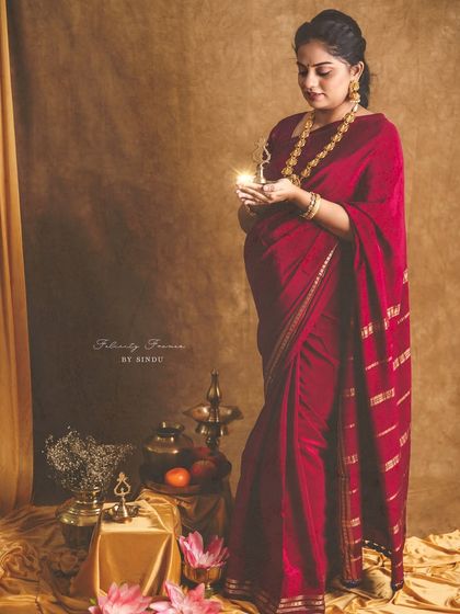 A beautiful portrait of an expectant mother in a red saree, holding a lit diya. The warm light and traditional setting create a serene and spiritual atmosphere for this maternity photo.