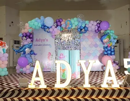 The main stage for the mermaid-themed party, with a silver sequin wall, a scale-patterned backdrop, and cutouts of Ariel and a seahorse.