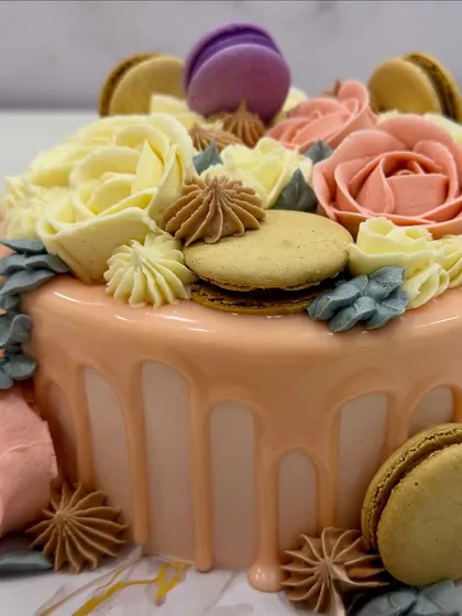 A close-up of one of the three cakes from the celebration: a vanilla sponge with white chocolate ganache, buttercream roses, a white chocolate drip, and macarons.