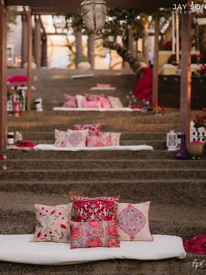 Unique tiered seating for the Mehfil-e-Mehendi, where mattresses and vibrant cushions are placed on stone steps, creating a relaxed and communal amphitheater-style lounge.