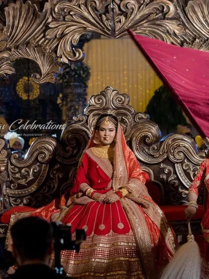A regal bride seated on an ornate golden palanquin for her grand entry. The rich red of her lehenga and the intricate details of the throne create a picture of pure royalty.