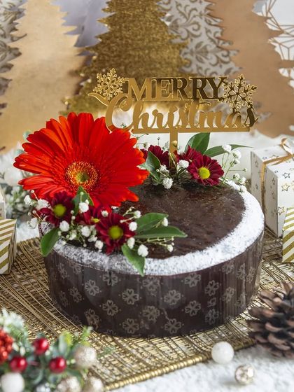 A classic Christmas plum cake decorated with a "Merry Christmas" topper and a fresh gerbera flower for a touch of elegance.