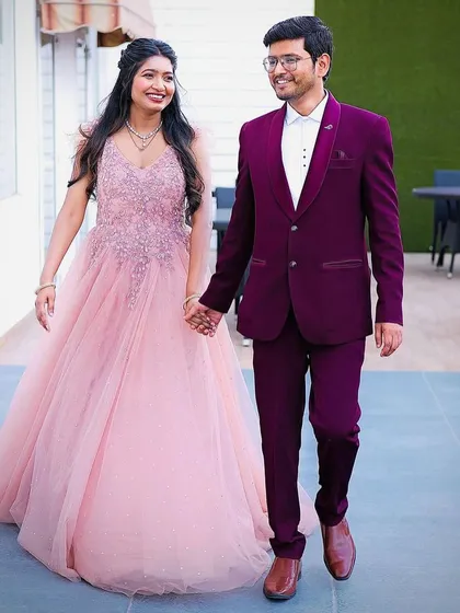 A closer look at the wine-colored tuxedo and pink gown combination. This pairing is perfect for couples who want a modern and romantic aesthetic for their reception or pre-wedding event. Notice the sharp cut of the suit and its rich color.