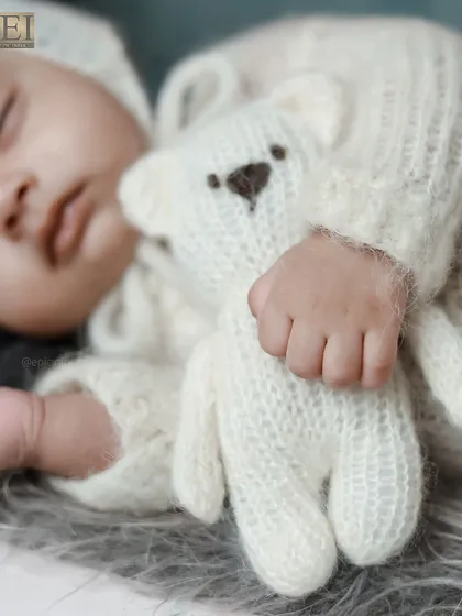 A close up shot capturing the peaceful sleep of a newborn. We focus on the tiny, delicate details, like their hands clutching a soft teddy bear, preserving the memory of just how small they once were.