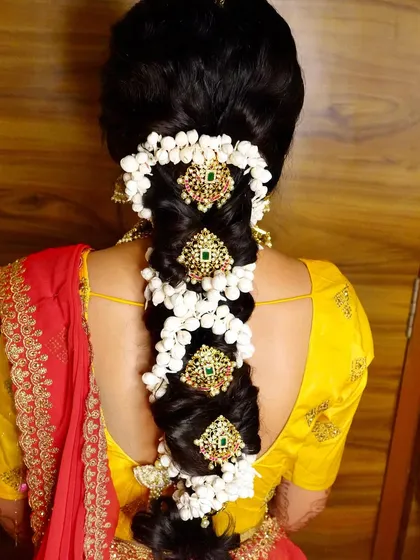 A detailed view of a South Indian bridal braid, decorated with mogra flowers and stunning green and gold hair ornaments.