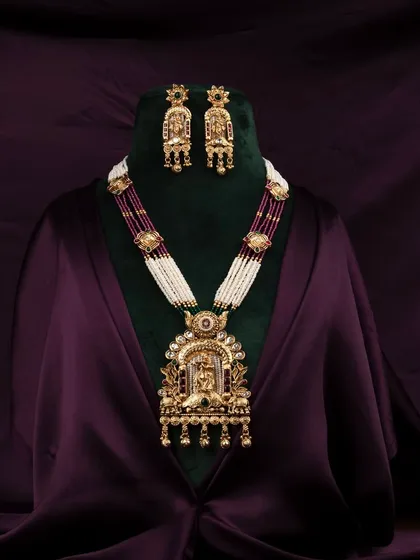 An opulent traditional Indian necklace and earring set, professionally displayed on a bust against a rich, dark purple satin background to highlight the intricate gold work and gemstones.