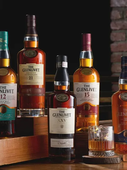 My personal favorite, The Glenlivet range. This shot captures the family of whiskies in a warm, rustic setting. The lighting is designed to feel like a cozy bar, with the brick wall and wooden shelf adding to the atmosphere.