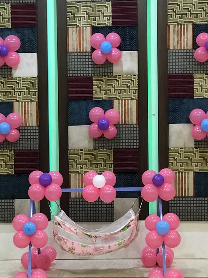 For a naming ceremony or newborn celebration, I offer this lovely cradle decoration. The rental includes the cradle stand decorated with pink balloon flowers against a textured wall panel.