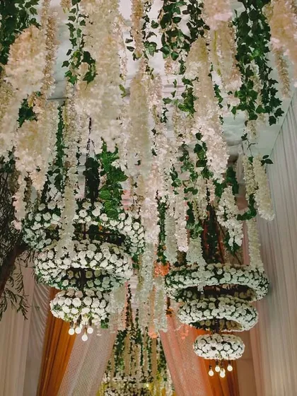 A closer look at the overhead details of the all-white stage. The hanging chandeliers are crafted from tiers of white carnations and delicate wisteria, adding depth and soft lighting to create a truly immersive and dreamy atmosphere.