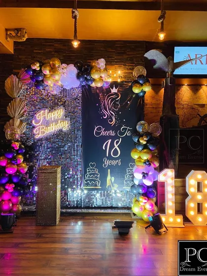 Another view of the stylish 18th birthday decor. The balloon arch in purple, black, and gold adds a festive touch to the glamorous sequin wall and custom signage.