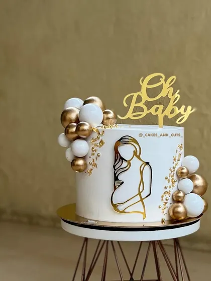 An elegant and modern baby shower cake. The design features clean, sharp edges, a gold silhouette, and delicate balloon clusters. Achieving that perfectly smooth buttercream finish is a core skill we focus on in all our hands-on cake decorating classes.