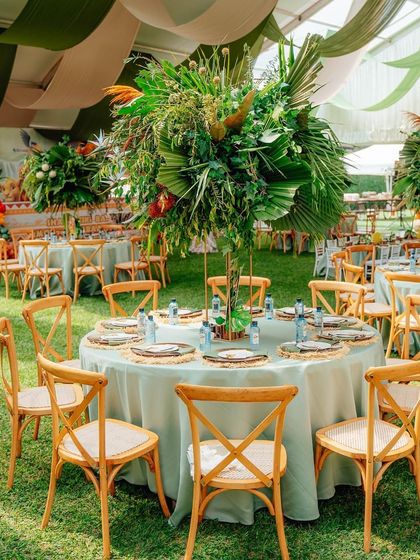 A stunning floral and foliage centerpiece designed for the guest tables. The arrangement uses large tropical leaves and greenery to enhance the jungle safari theme.