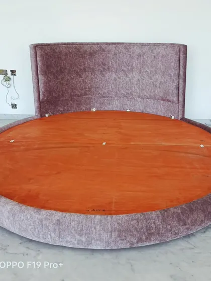 A special request for a custom-made round bed. This unique piece is fully upholstered in a textured fabric and is built on a strong wooden base.