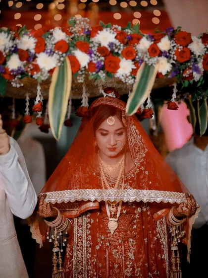 The bride's grand entrance under a 'phoolon ki chadar'. Her makeup is soft and ethereal, with a focus on glowing skin, matching the romantic mood.