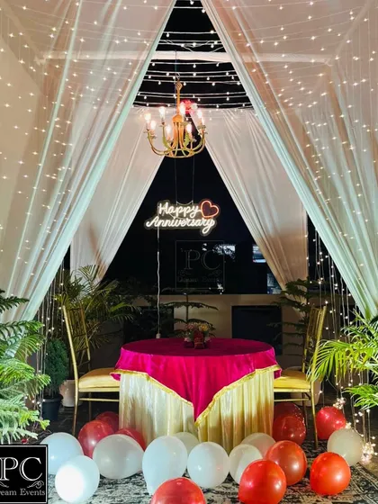 We create magical moments like this intimate anniversary dinner setup on a private terrace. A canopy of sheer white drapes, twinkling fairy lights, and a custom 'Happy Anniversary' neon sign make for an unforgettable romantic surprise.
