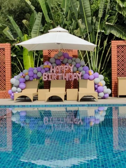We can decorate any space, even by the pool. This poolside birthday setup features a balloon garland in purple and grey with 'Happy Birthday' foil letters, creating a fun and festive vibe.