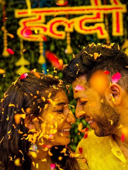 A sweet moment of a couple during their haldi, with flower petals falling around them against a backdrop of marigolds.