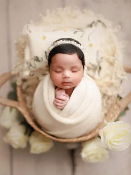 The sweetness of new beginnings. An all-white setup with white roses creates a pure and classic look for this beautifully wrapped newborn in a basket.