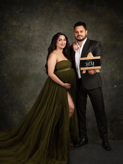 A proud gender reveal moment for the couple. They hold up an 'It's a Boy' sign, sharing their happy news in this stylish and classic studio portrait.