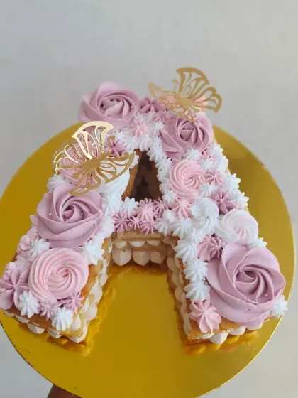 A beautiful "A" initial tart cake, decorated with piped rosettes and golden butterflies.