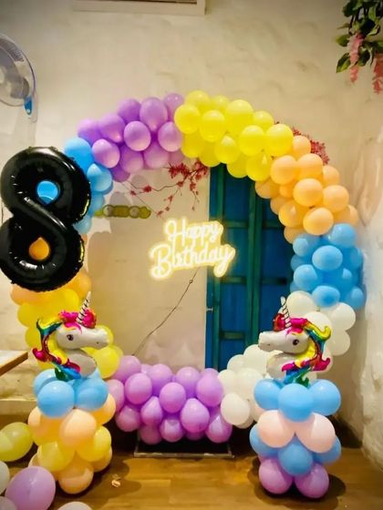 A magical unicorn-themed birthday party with a rainbow balloon arch. This setup includes unicorn-shaped balloon pillars and a neon sign, perfect for an 8th birthday celebration.