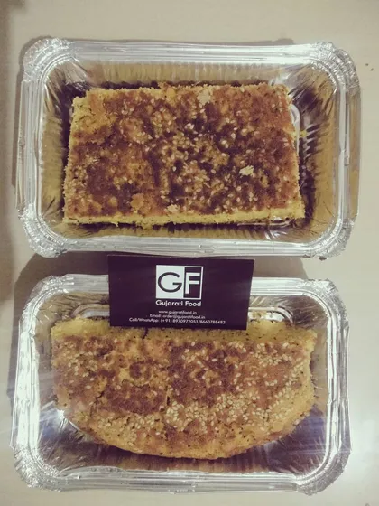 This is Handvo, a traditional savory cake made from rice, lentils, and vegetables like bottle gourd. It's baked until golden and is a wholesome, nutritious snack, delivered in convenient foil containers.