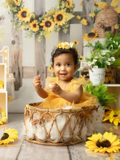 A happy little bee in a field of sunflowers. This shot shows the full setup, complete with a wicker basket and floral details, creating a perfect scene for a first birthday portrait.