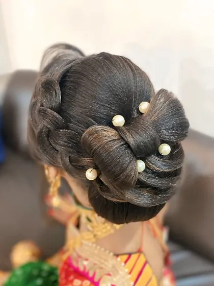 A unique updo featuring a combination of a braid and a knotted bun. The look is finished with pearl pins, adding a touch of sophistication to this intricate hairstyle.