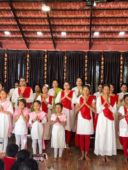 A large group of my students on stage, united in a prayerful 'namaskar' pose, representing the diverse and growing family at Sāttvatī.