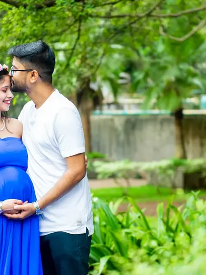 A tender moment between partners. The dad-to-be gently kisses his partner's forehead as she glows in a vibrant blue dress.