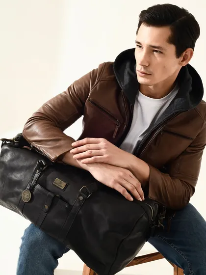 A commercial portrait for Kompanero, showcasing a leather jacket and travel bag. The look is rugged yet stylish.