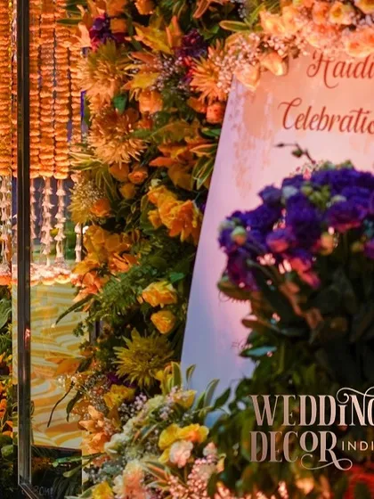 The welcome signage for the Haldi celebration, nestled within a lush floral arrangement. The warm lighting makes the sign glow, creating an inviting entrance.