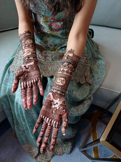 A detailed view of personalized bridal mehndi, featuring a couple's story with initials and symbolic figures.