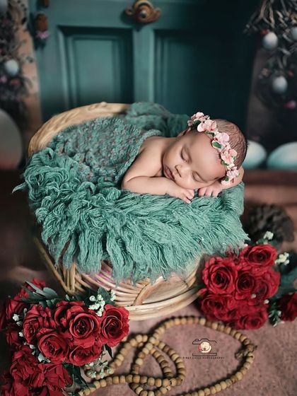 A cozy basket pose with beautiful color contrast. The baby sleeps on a soft teal blanket, surrounded by rich red roses, creating a visually striking and peaceful newborn photograph.