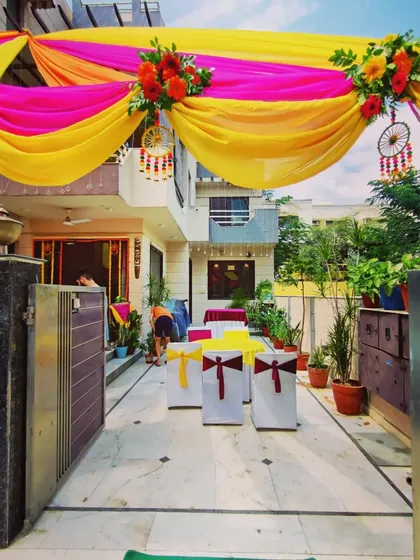 A closer view of the entrance area for a Mehandi and Sangeet function. The draped canopy is accented with floral bouquets and dreamcatchers, and chairs are set up for guest seating.