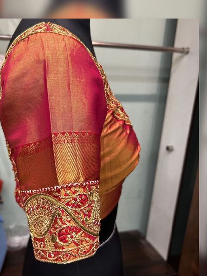 A side view of the red and gold blouse, focusing on the puff sleeve and the heavily embroidered cuff.