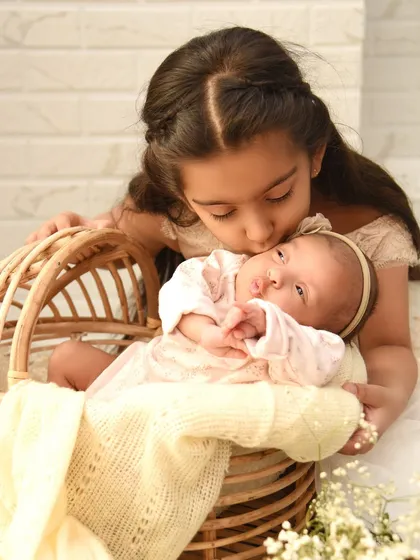 A tender moment between two sisters. The older sister gently kisses her newborn sibling, capturing the beginning of a lifelong bond. We focus on creating a comfortable space for these quiet, precious interactions to happen naturally.