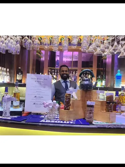 A fully stocked bar ready for service. This wide shot shows the extensive selection of spirits, glassware hanging from above, and our bartender ready to welcome guests.