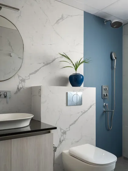 The bathroom design combines classic marble-look tiles with a bold blue accent wall in the shower area. This creates a fresh, modern look that is both luxurious and easy to maintain.