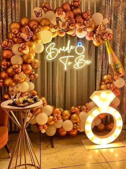 A full circle balloon arch in chrome gold and white, paired with a neon sign and a light-up prop, makes for the ultimate bachelorette party backdrop.
