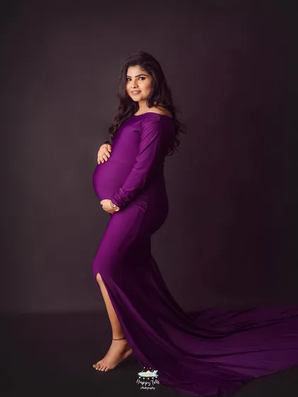 We love a bold color choice. This stunning off-the-shoulder purple gown creates such a striking and powerful silhouette, beautifully highlighting the baby bump against a classic dark backdrop.