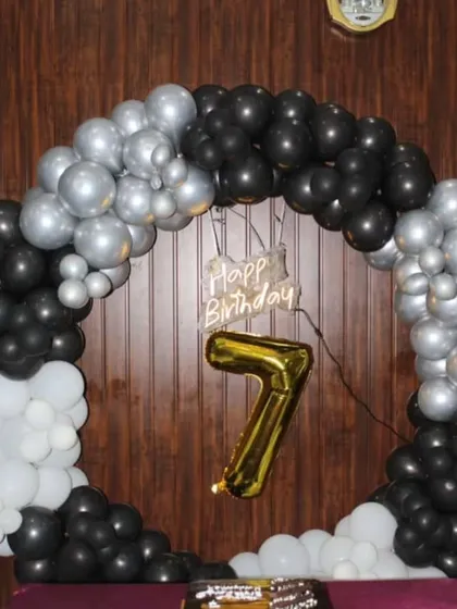 A sleek black, silver, and white circular balloon arch for a 7th birthday. A large gold foil number '7' hangs in the center, creating a modern and stylish look.