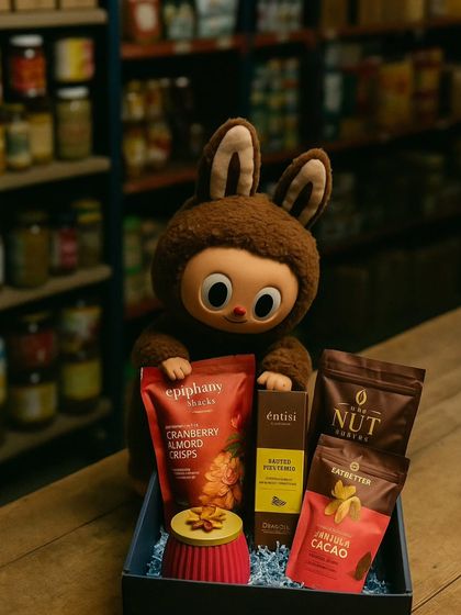 Another shot from my imagined world where Labubus run the studio. Here, a brown Labubu carefully arranges a hamper filled with cranberry almond crisps and other gourmet snacks.