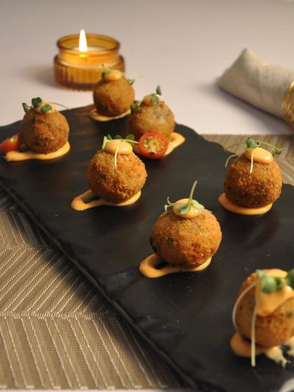 These are my crispy Arancini Balls, served on a slate platter with a drizzle of sauce and microgreens. They are a perfect bite-sized appetizer for festive occasions like Diwali, offering a gourmet touch to your party menu.
