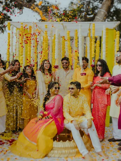A fun group photo from a Haldi ceremony, with the couple and their friends celebrating with a shower of flower petals.