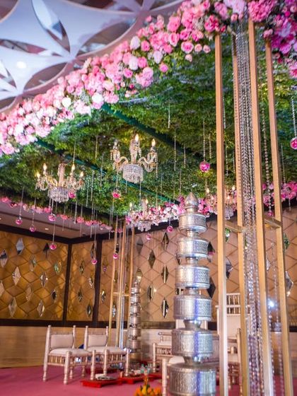 This mandap is a beautiful fusion of themes, with a ceiling of pink flowers and lush greenery, silver pillars, and a backdrop of mirrored walls.